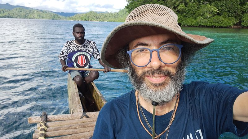 Gianluca Grimalda macht ein Selfie von sich auf einem Ruderboot. Hinter ihm sitzt eine Person mit einem Ruder am Heck über dunkelblaubem Wasser.
