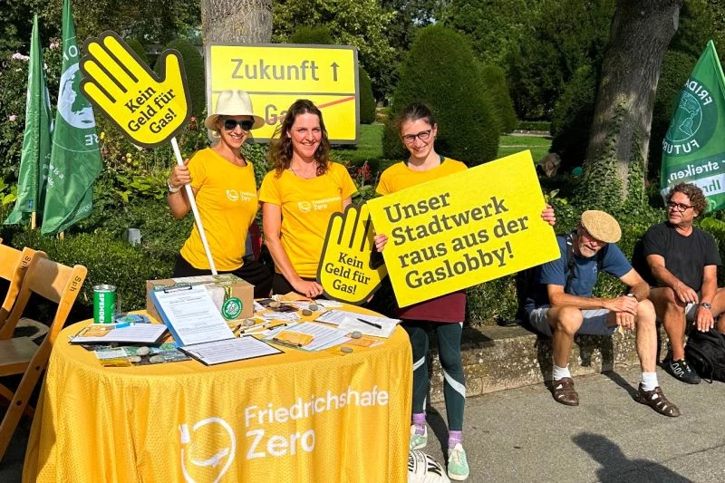 Orange gekleidete Menschen demonstrieren an einem Infostand mit Schildern wie: Unser Stadtwerk raus aus der Gaslobby!