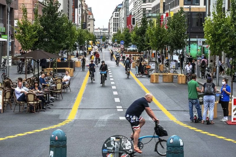 Auf der autofreien Friedrichstraße sitzen Menschen an Cafétischen, in der Mitte fahren Leute mit dem Fahrrad.