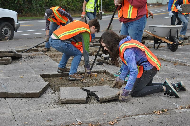 Junge Leute in Warnwesten brechen große Platten aus einem gepflasterten Gehweg in Tacoma bei Seattle.