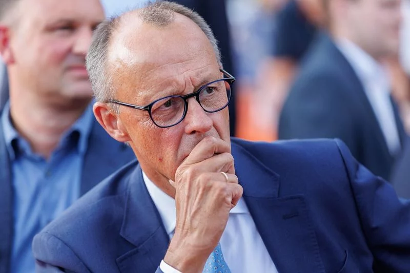 Friedrich Merz in Großaufnahme bei einer Veranstaltung, sein Gesichtsausdruck bewegt sich zwischen aufmerksam, nachdenklich und zweifelnd-distanziert.
