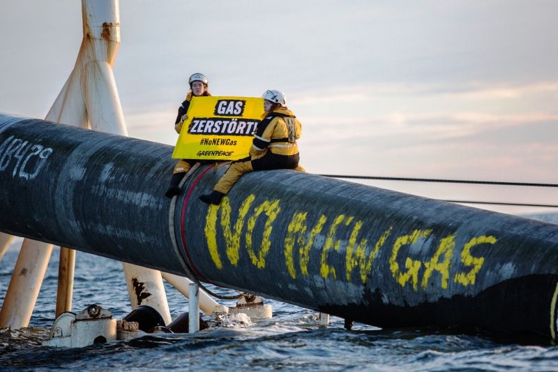 Zwei Aktivistinnen sitzen auf einer zwei Meter dicken Pipeline, die am Heck des Verlegeschiffs zu Wasser gelassen wird. Auf die Pipeline haben sie auf Englisch geschrieben: Kein neues Gas.