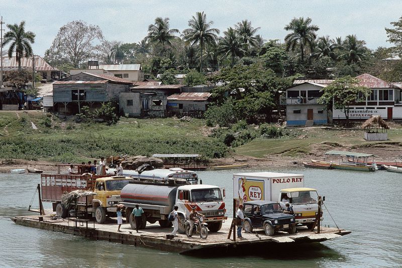 Eine kleine Fähre mit einigen Fahrzeugen fährt über den Fluss La Pasión im Ort Sayaxché bei Flores in Guatemala.