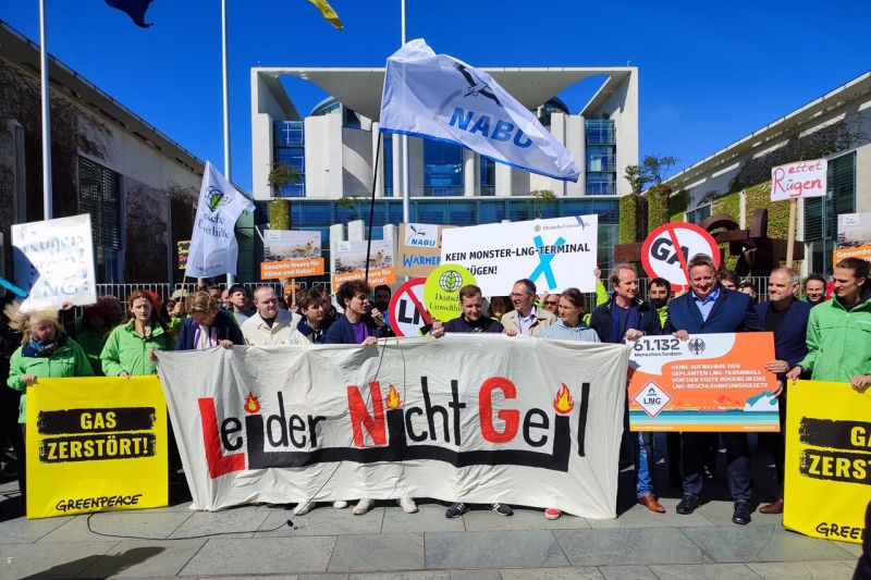 Zwei Dutzend Menschen stehen mit vielen bunten Schildern, Fahnen und Transparenten vor dem Bundeskanzleramt in Berlin.