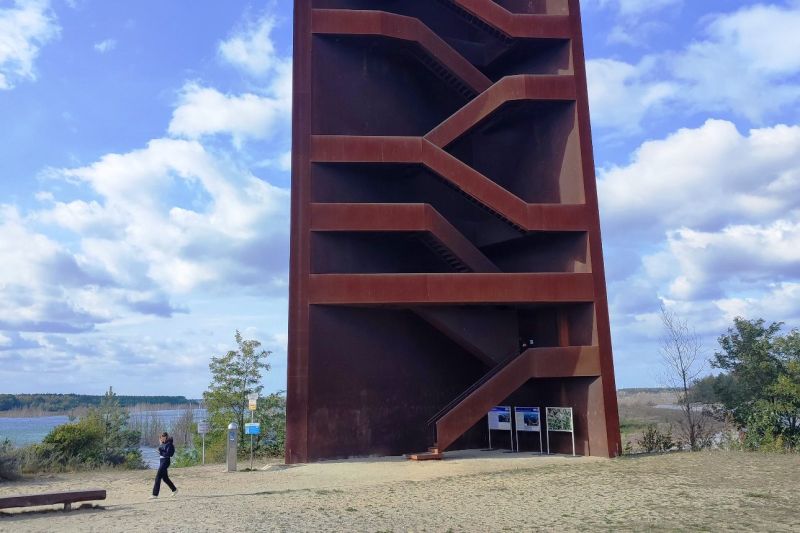 Ein Turm aus rostigem Stahl steht in einer kargen Landschaft.