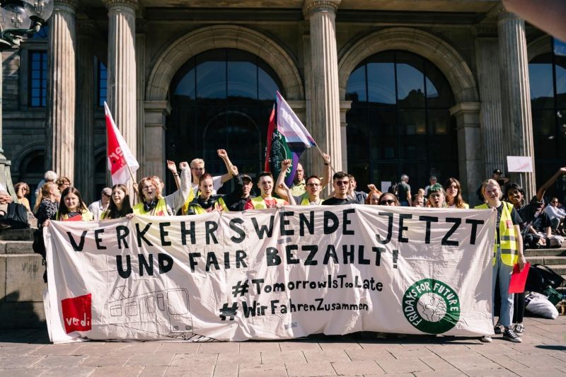 Junge Leute stehen hinter einem Transparent mit den Logos von Verdi und Fridays for Future und der Aufschrift: Verkehrswende jetzt und fair bezahlt!