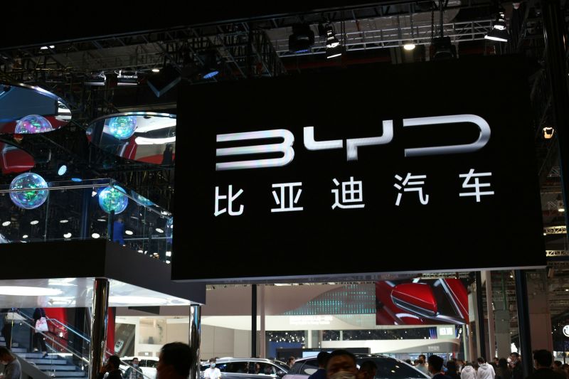 Menschen schauen sich auf einer Ausstellung neue Autos an, über ihnen ein riesiges schwarzes Schild mit der Automarke: BYD, Autohersteller aus China.