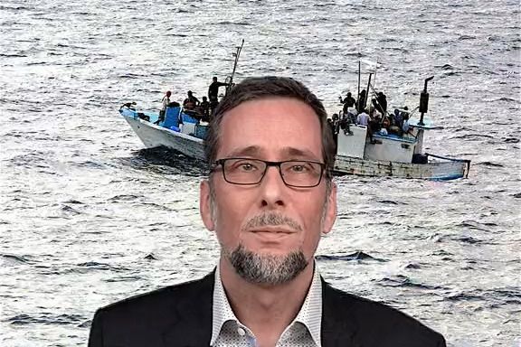 Volker Quaschning im Anzug, hinter ihm ein Foto von einem kleinen Flüchtlingsschiff im Meer.
