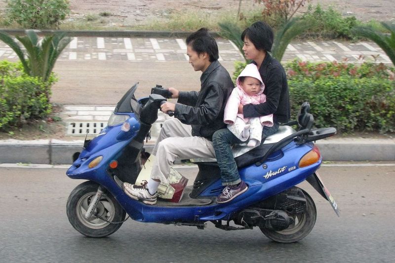 Eine dreiköpfige chinesische Familie fährt auf einem leichten Motorroller.