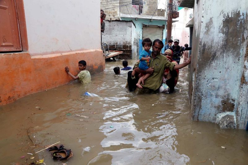 Bewohner der pakistanischen Hafenstadt Karatschi waten durch hüfthohes, braun gefärbtes Wasser.