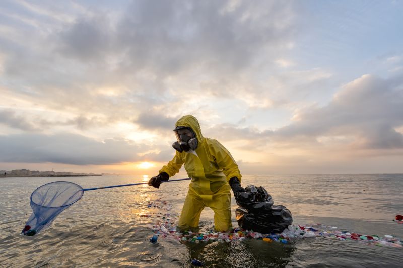 Eine Person im gelben Schutzanzug und mit Schutzmaske sammelt bei einer Freiwilligen-Aktion Plastikmüll aus dem Meer.