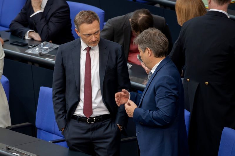 Christian Lindner schaut skeptisch und hält die Hände in den Hosentaschen, während Robert Habeck zu ihm spricht und mit den Händen gestikuliert. Beide stehen an der Regierungsbank im Bundestag.
