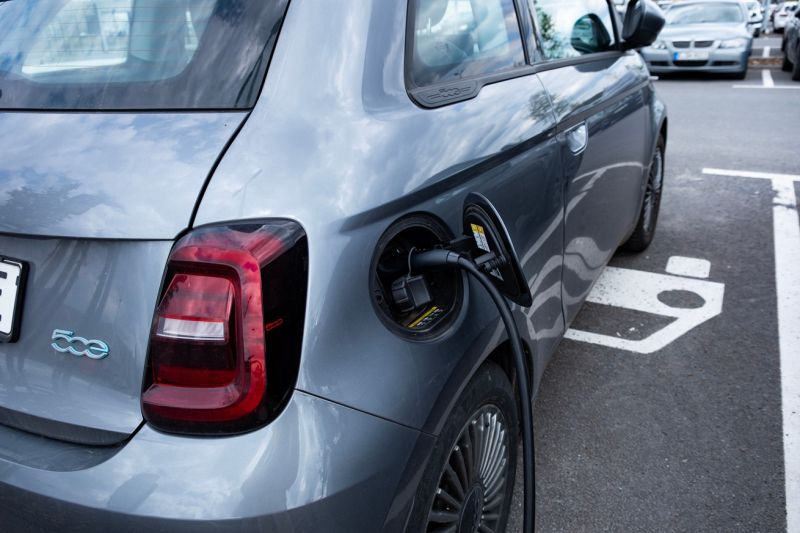 Ein Kleinwagen Fiat 500 steht auf einem Parkplatz und wird aufgeladen.