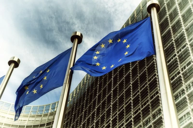 Vor dem Sitz der EU-Kommission in Brüssel wehen einige Europafahnen im starken Wind, am Himmel sind Gewitterwolken zu sehen.