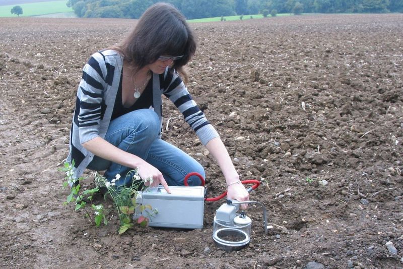 Eine Wissenschaftlerin hockt auf einem Feld und misst die Bodenfeuchte mit einem Messgerät.