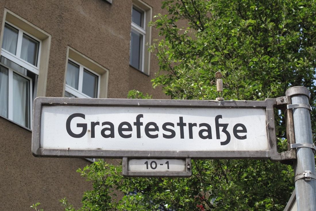 Straßenschild für die Graefestraße, im Hintergrund ein einfach verputztes Mietshaus mit Plastikfenstern.