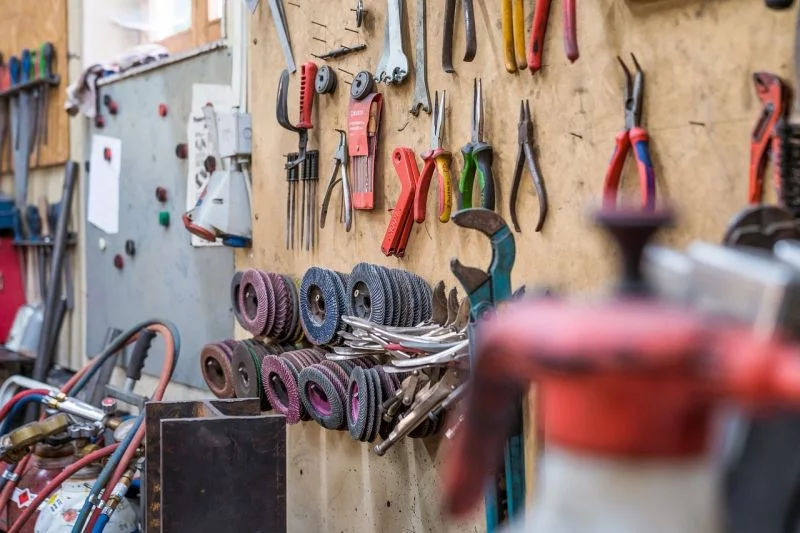 Zangen, Schleifscheiben und anderes Werkzeug hängen in einer Werkstatt an der Wand.