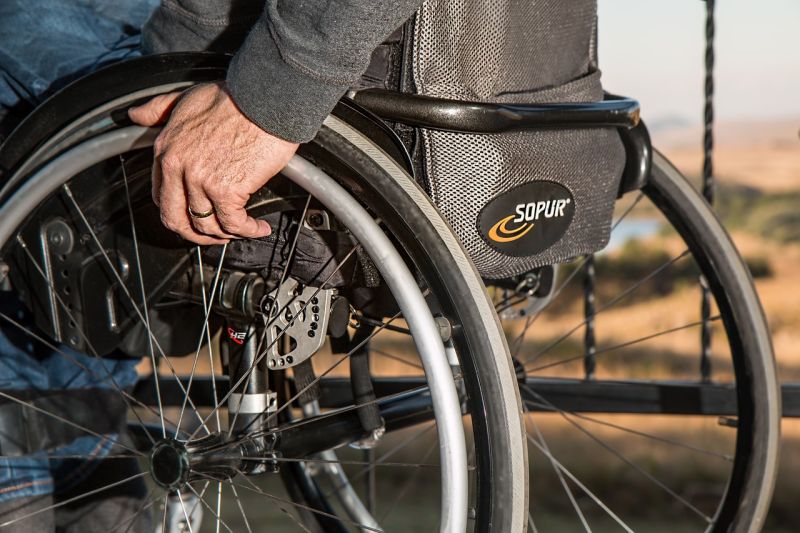 Ein älterer Mensch im Rollstuhl, man sieht vor allem eine Hand und die Räder.