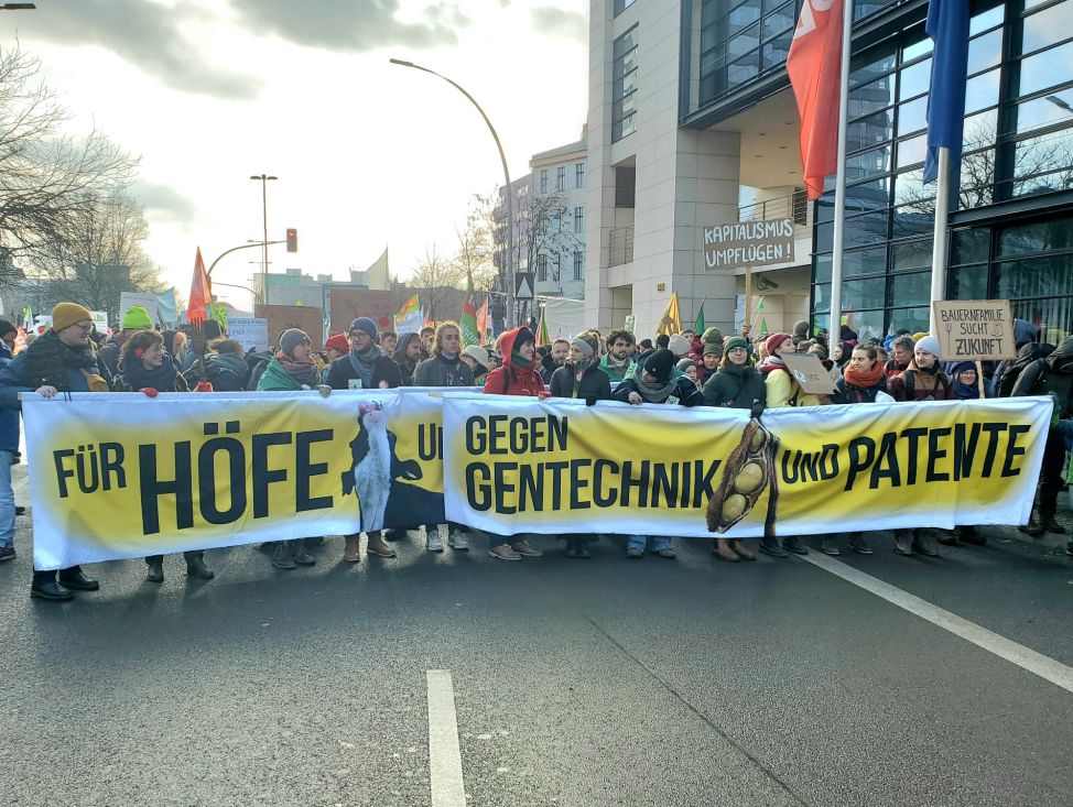 In der vordersten Reihe des Demozugs halten Menschen ein Banner mit der Aufschrift: Für Höfe und Klima - gegen Gentechnik und Patente.